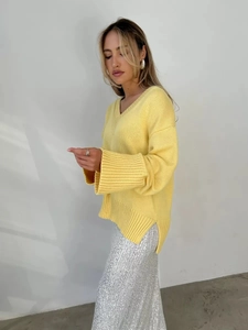 Dettaglio del maglione in maglia gialla con scollo a V, spalle scese e polsini a coste