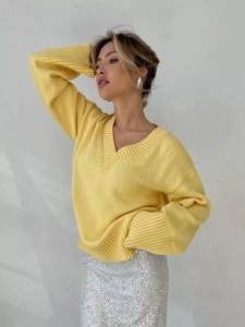 Dettaglio ravvicinato di un maglione giallo con scollo a V, polsini a coste e gonna glitter
