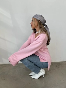 Dettaglio della trama a maglia grossa e dello spacco laterale del maglione rosa a V