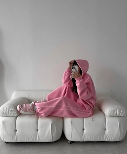 Detail of pink athleisure hoodie and side-stripe sweatpants set on a white sofa