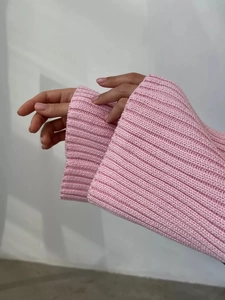 Dettaglio del polsino di un maglione a coste rosa che mostra la consistenza morbida del tessuto