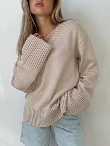 Dettaglio del maglione beige con scollo a V che mostra la trama e i polsini a costine