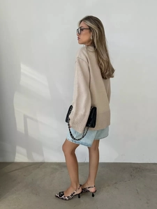 Dettaglio laterale di un maglione oversize beige con scollo a V e polsini a costine