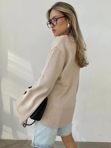 Dettaglio di un maglione di maglia beige oversize con polsini a coste e spalla scesa