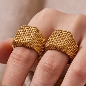 Close-up of square gold rings with intricate beaded texture on a person's finger