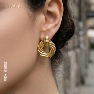 Detail of twisted gold earrings in titanium steel worn by a model in warm light