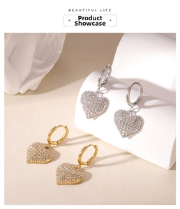 Detailed view of gold and silver heart-shaped zircon drop earrings on a minimalist pedestal