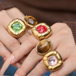 Close-up of hand wearing chunky gold titanium rings with emerald and tiger eye stones