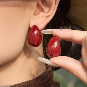 Close-up of bright red teardrop resin earrings with hoop design worn by a model