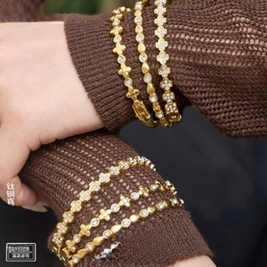 Detail of 18k gold plated titanium clover bracelets on a brown knitted sweater sleeve
