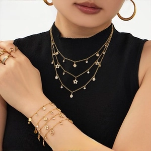 Close-up of gold layered necklace and bracelet set with white zircon flower pendants