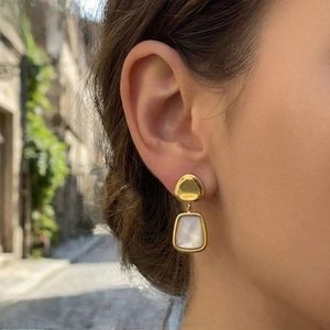 Close-up of dangling gold-plated earrings with white stones worn by a model