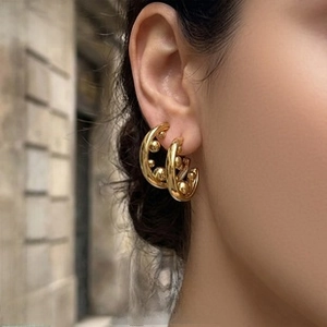 Close-up of golden beaded hoop earrings on model with titanium steel plating