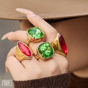 Detail of stacked wide gold rings with green cushion-cut and red marquise gemstones