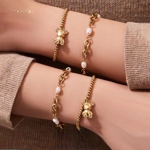 Detail of layered gold bear pendant bracelet and pearl chain on a knit sleeve