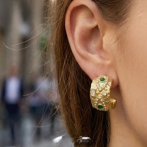Detail of vintage C-shape gold earrings with hammer texture and green oval gemstones
