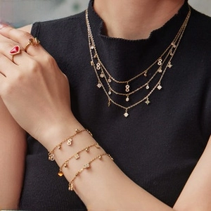 Close-up of a layered gold necklace and bracelets with a red heart gemstone ring on female