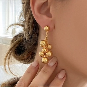 Close-up of a model wearing 18k gold plated drop earrings with a cluster of polished spheres
