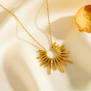 Detailed view of an 18K gold sunray pendant on silk fabric with vintage autumn leaves