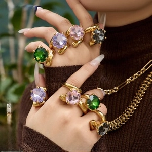 Close-up of 18K gold plated rings with large colorful gemstones on a brown sweater