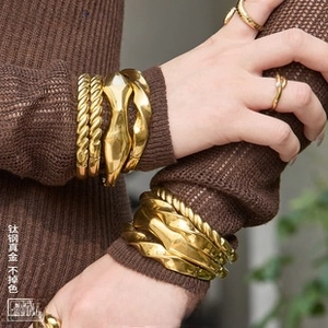 Detail of layered gold titanium steel bracelets and rings featuring a twisted rope design