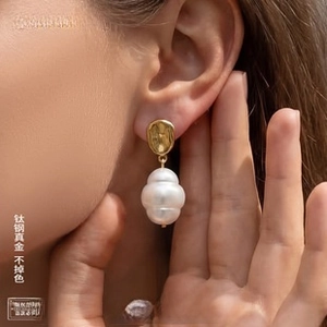 Detail of gold hammer-textured titanium earrings with baroque pearl on model