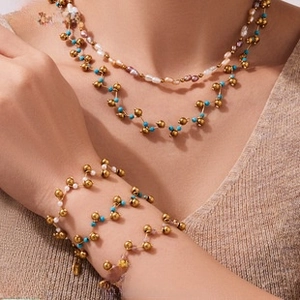 Layered gold beaded necklaces and bracelets with white pearls and turquoise on model