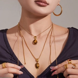 Detail of model wearing 18K gold plated pearl earrings and layered snake chain necklace