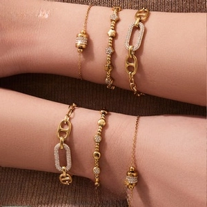 Detail of layered gold-plated bracelets with cubic zirconia and oval link chain on wrist