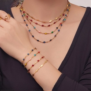 Detail of layered gold necklaces and bracelets with colorful enamel charms on model
