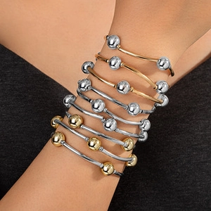 Stackable gold and silver metal bangles with polished round beads shown on a model wrist