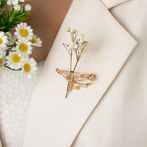 Detail of golden branch brooch pin holding white dried flowers on a white suit lapel