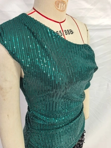 Dettaglio di paillettes verde scuro luccicanti su un elegante abito monospalla da sera