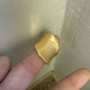 Macro shot of wide gold wavy ring showing polished mirror surface and irregular edges