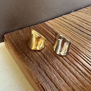 Close-up of minimalist gold and silver wide wavy rings on a rustic wooden base