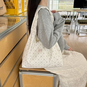 Detail of white canvas tote bag with green bow print and quilted texture on model