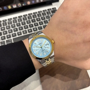 Close-up of men's watch featuring light blue textured dial and gold fluted bezel detail