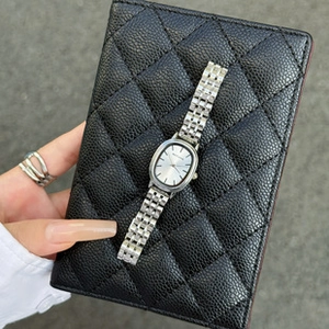 Silver oval quartz watch with metal mesh strap shown against a black quilted background