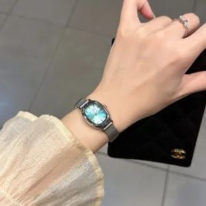 Detail of a silver mesh strap watch with a blue sunray oval dial on a woman's wrist