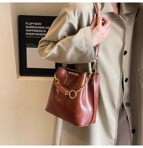 Detail of vintage brown bucket bag with gold chain and fashion tag on beige trench coat