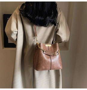 Detail of a brown bucket bag with gold chain and shoulder strap shown in a lifestyle scene