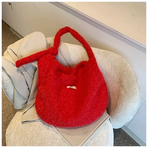 Close-up of vibrant red plush crescent tote bag with knot detail on ivory chair