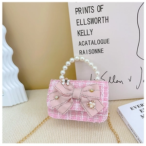 Close-up of pink tweed girl handbag featuring large bow, pearls, and gold chain strap