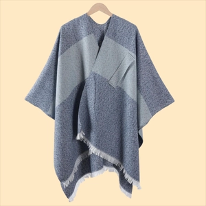 Detail eines graublauen Strickponchos mit geometrischen Farbfeldern und weißen Quasten