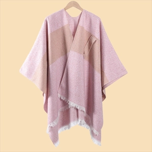 Detail eines weichen Strickponchos in Rosa und Beige mit weißen Fransenquasten