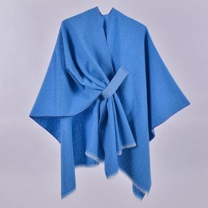 Dettaglio dello scialle blu in maglia con nodo incrociato anteriore e bordi con frange bianche