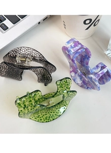 Close-up of three large acetate claw clips in black, purple, and green on a desk