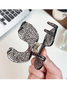 Close-up of black and white marbled acetate hair claw clip held by hand in home setting