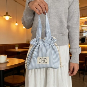 Détail du sac à cordon en toile rayée bleue avec broderie nœud et logo de marque