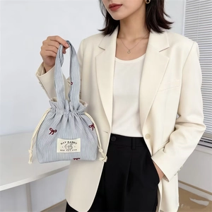 Détail du sac à cordon en toile rayée bleue avec nœud brodé rouge et étiquette lapin